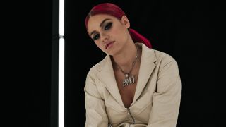 Rapperin Badmómzjay sitzt mit zur Seite geneigtem Kopf vor einer schwarzen Wand mit einer Neonröhre. (Quelle: Jesko Gorgas)