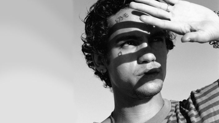 Musiker Dominic Fike hält seine linke Hand vor die Hälfte seines Gesichts, um ein bisschen Schatten im Gesicht von der Sonne zu haben. Das Bild ist schwarz weiß und er guckt in die Ferne. | Quelle: Universal Music