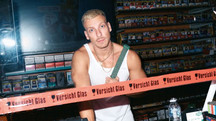 Felix steht im Unterhemd hinter einem Absperrungsband in einem Späti | Quelle: Marvin Ruppert Felix steht im Unterhemd hinter einem Absperrungsband in einem Späti | Quelle: Marvin Ruppert