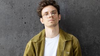 Tim Kamrad lehnt in einer grünen Jacke an einer grauen Betonwand. (Quelle: Bella Lieberberg)