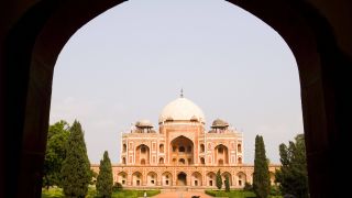 Blick durch ein Tor ohne Türen auf ein prunkvolles Gebäude, das in einem Park steht in Neu-Delhi.| Quelle: IMAGO / Avalon.red