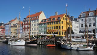 Alte Häuser in Kopenhagen direkt am Fluss. Auf dem Fluss befinden sich mehrere Boote. Die Sonne scheint. | Quelle: IMAGO / Dean Pictures