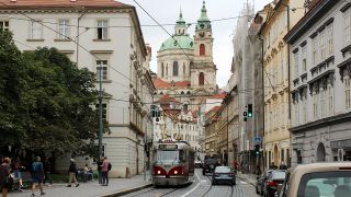 Die Prager Innenstadt. Es sind alte, verschnörkelte Häuser zu sehen und dazwischen eine alte Tram. Menschen laufen durch die Straße. | Quelle: IMAGO / CTK Photo