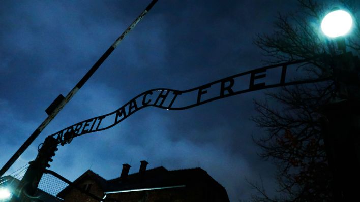 Der Eingang des Konzentrationslager Auschwitz mit dem Schriftzug "Arbeit mach frei", dahinter düsterer Himmel (Quelle: IMAGO | Nur Photo)
