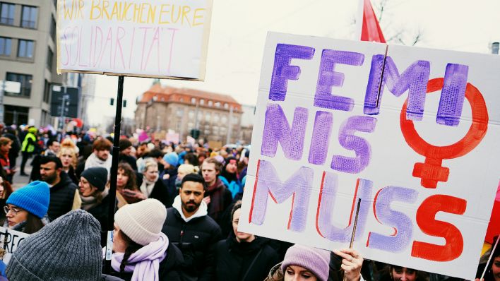 Eine Demo in Berlin. Menschen halten Schilder in die Höhe. Eins ist rechts im Vordergrund mit der Aufschrift "Feminismuss". | Foto: IMAGO / snapshot