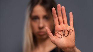 Ein Frau hält ihre Hand mit dem Wort "Stop" draufgeschrieben in die Kamera. (Quelle: IMAGO | MiS)