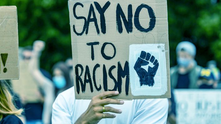 Jemand hält ein Schild mit der Aufschrift "Say no to Racism" hoch (Quelle: Imago | Arnulf Hettrich)