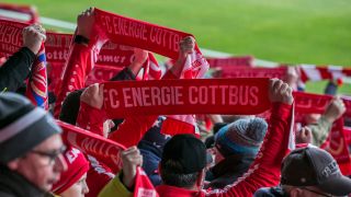 Energie-Cottbus-Fans halten ihren Schal im Stadion hoch (Quelle: IMAGO | Fotostand)