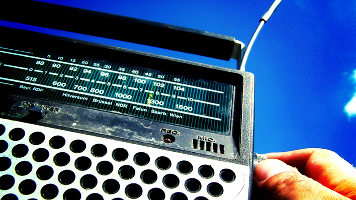 Ein Radio, an dessen Regler eine Hand dreht, vor blauem Himmel (Foto: spacejunkie l photocase.com)