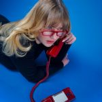 Die Musikerin Dilla telefoniert mit roter Brille und einem roten analogen Telefon. (Quelle: Lola Schreiner)