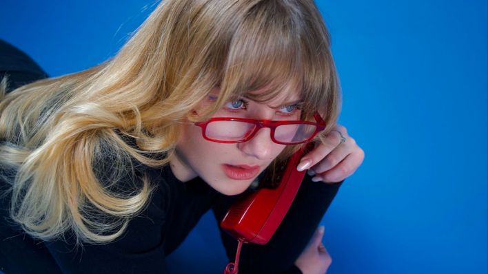 Die Musikerin Dilla telefoniert mit roter Brille und einem roten analogen Telefon. (Quelle: Lola Schreiner)