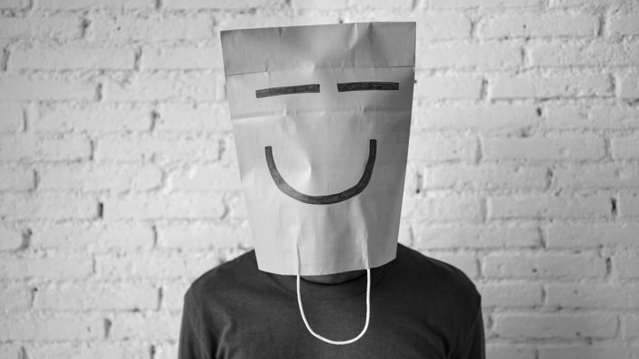 Eine Person, die sich eine mit einem Smiley bemalten Papiertüte über den Kopf gezogen hat. (Quelle: IMAGO | Westend61)